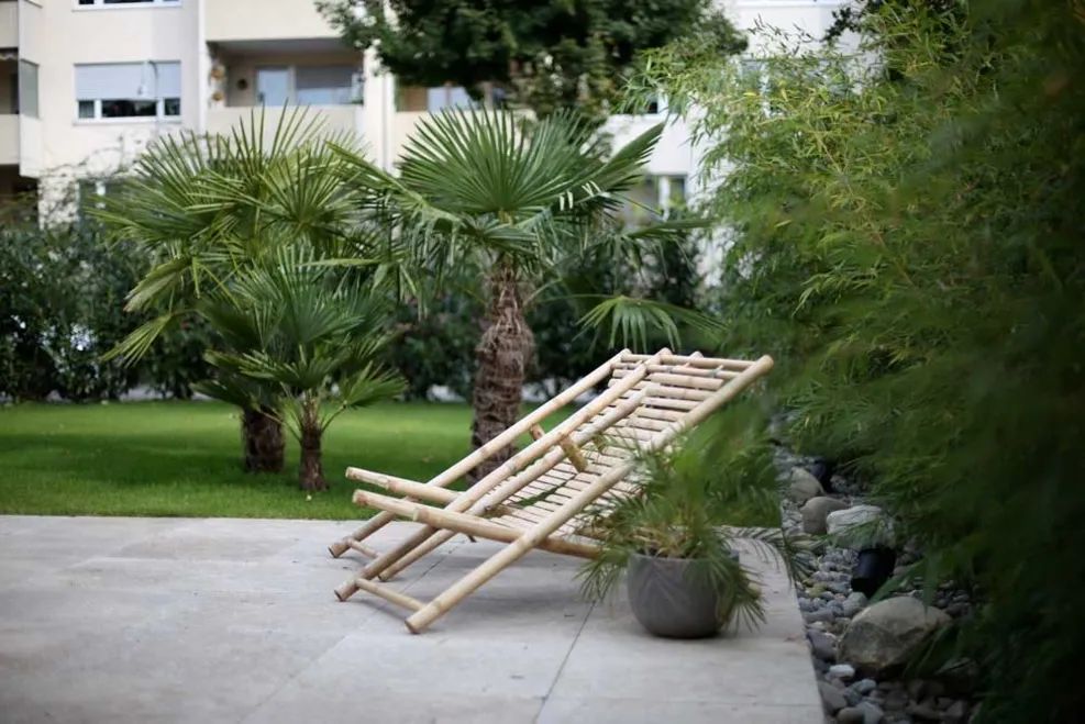 Garten mit Palmen und Holzliege auf hellem Belag