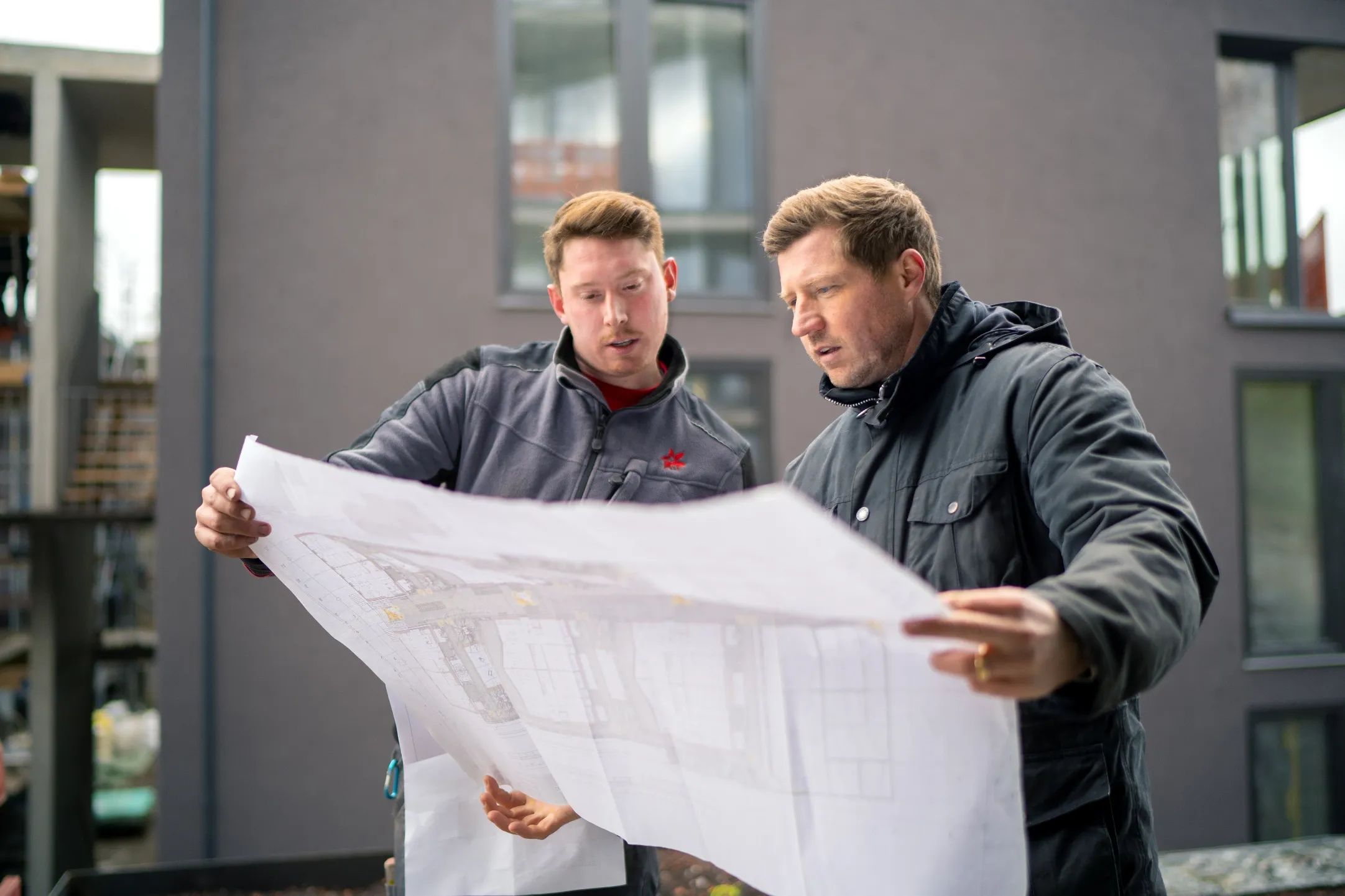Zwei Mitarbeiter von Steidle besprechen einen Plan vor einem Gebäude